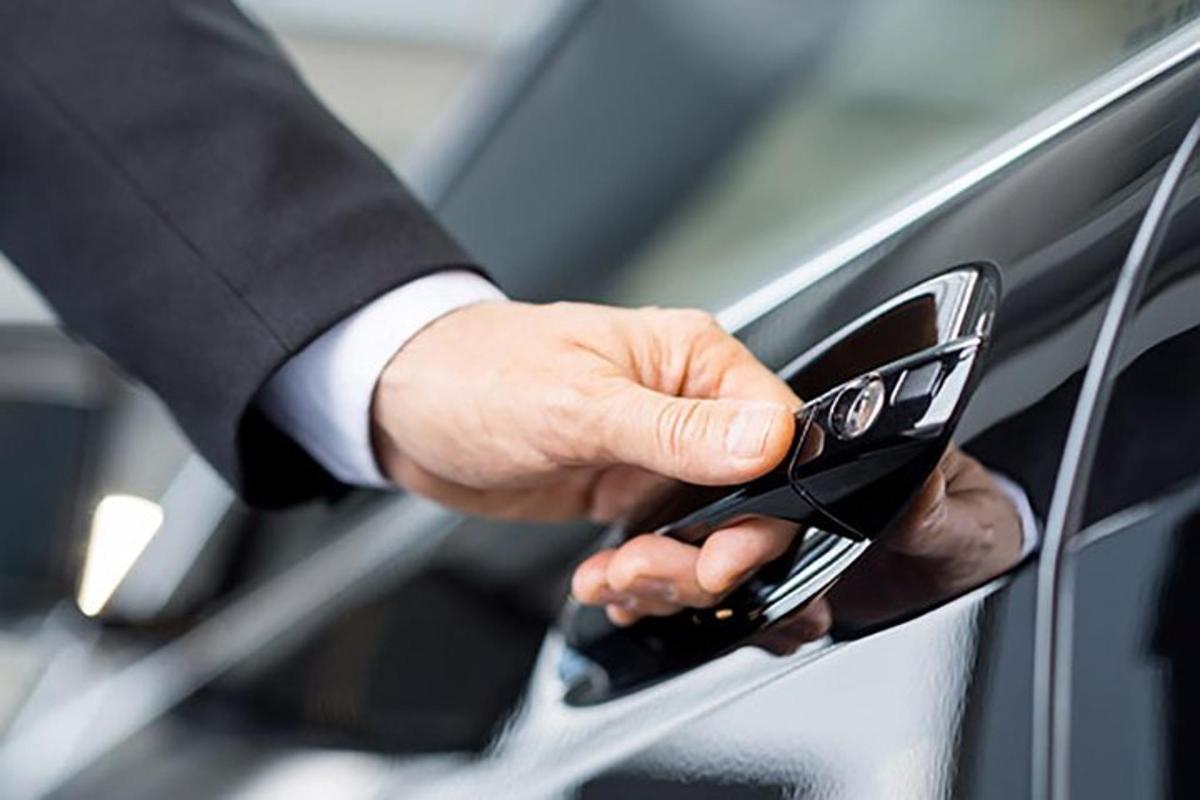 ülikonnas mees hoiab mobiiltelefoni auto vastas
