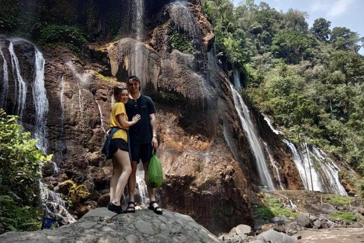 a man and a woman standing on a rock in front of a waterfall