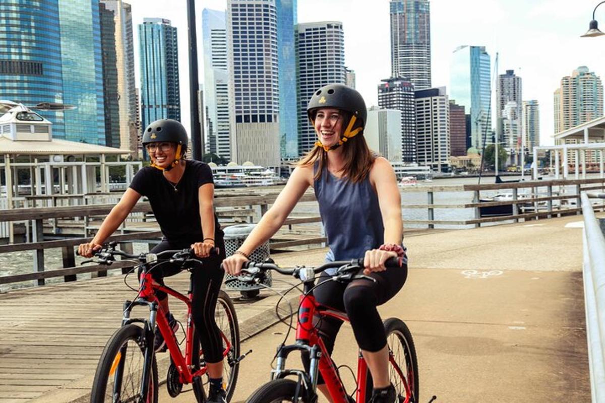 two women wearing helmets riding bikes on a bridge