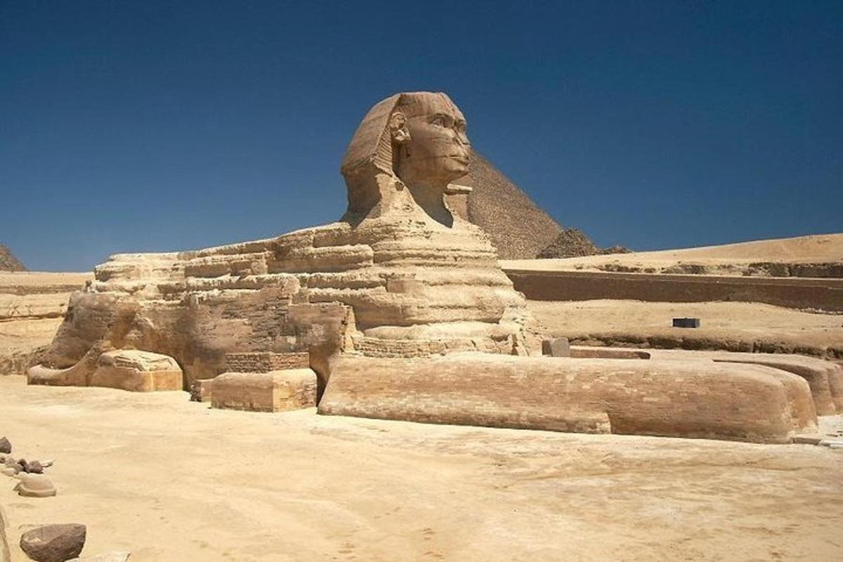uma estátua no deserto com uma pirâmide ao fundo