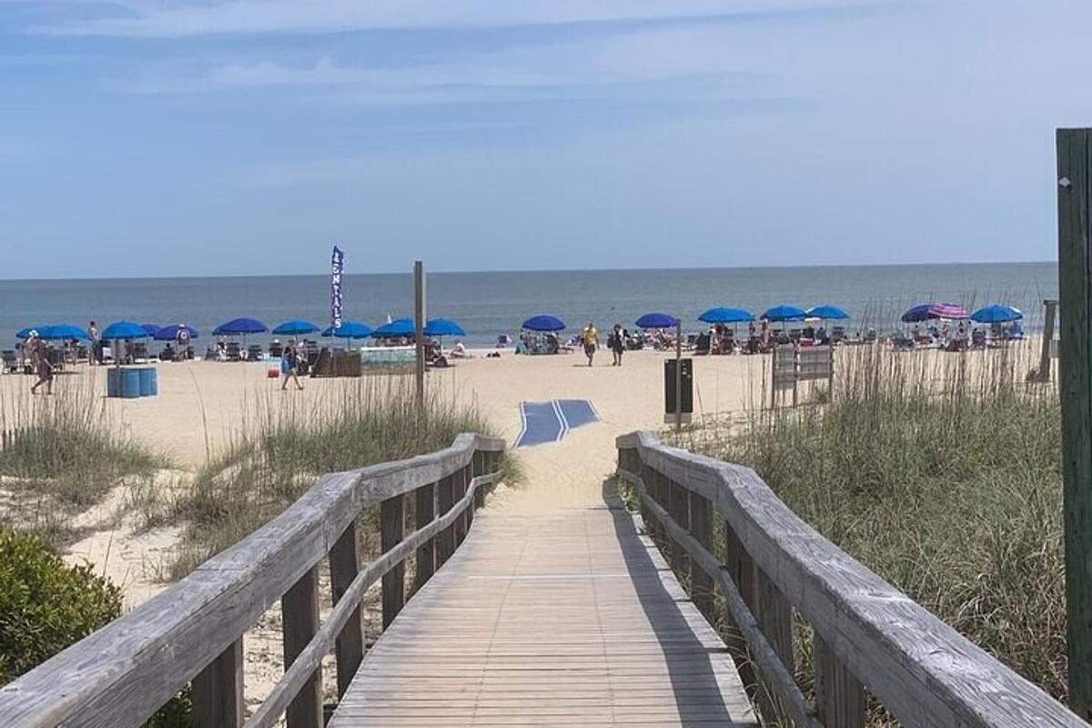 ein Holzsteg, der zum Strand mit Sonnenschirmen führt