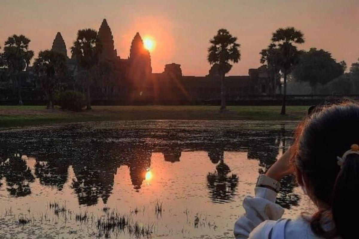 a woman taking a picture of the sunset in front of a lake