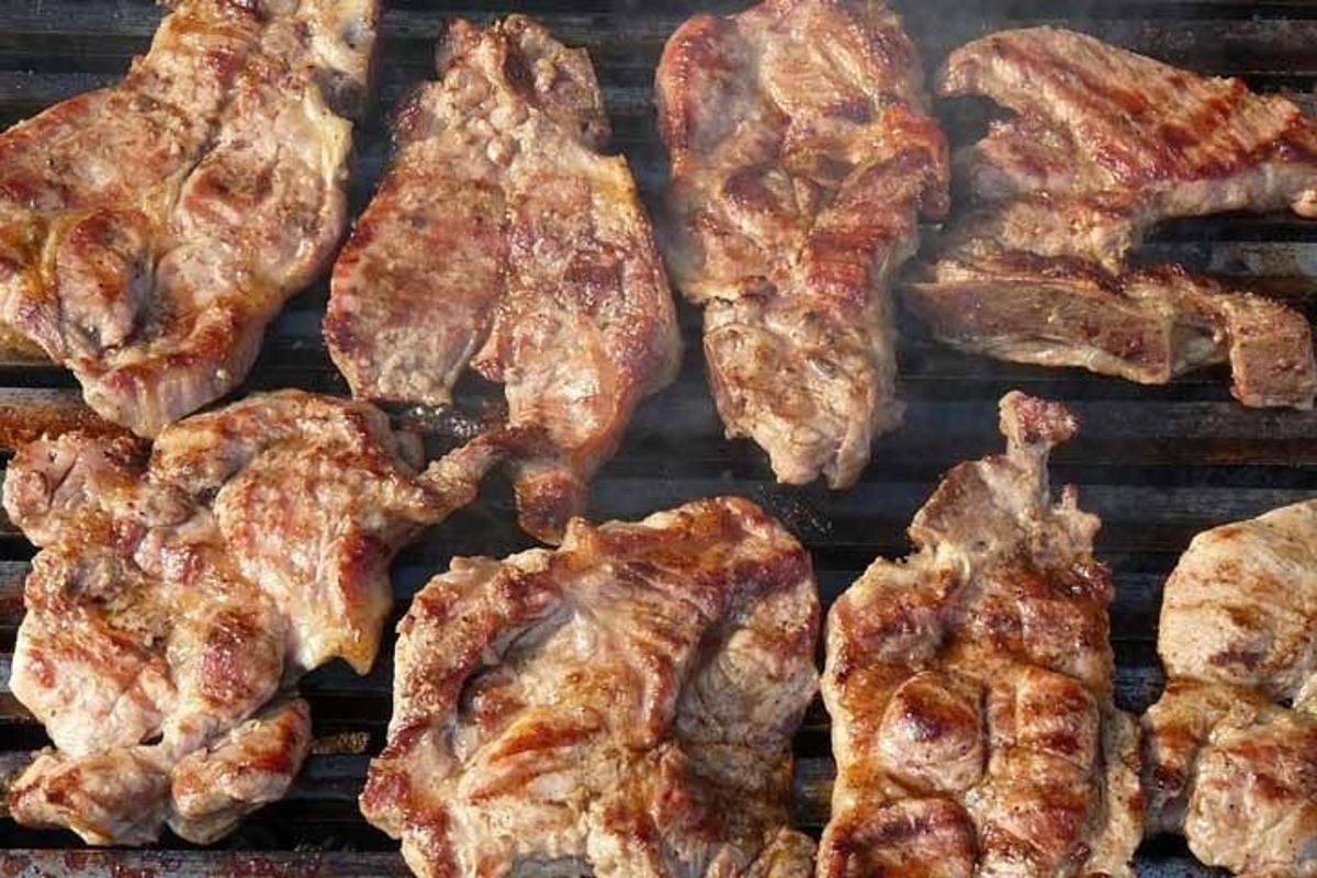 Un montón de carne cocinándose en una parrilla