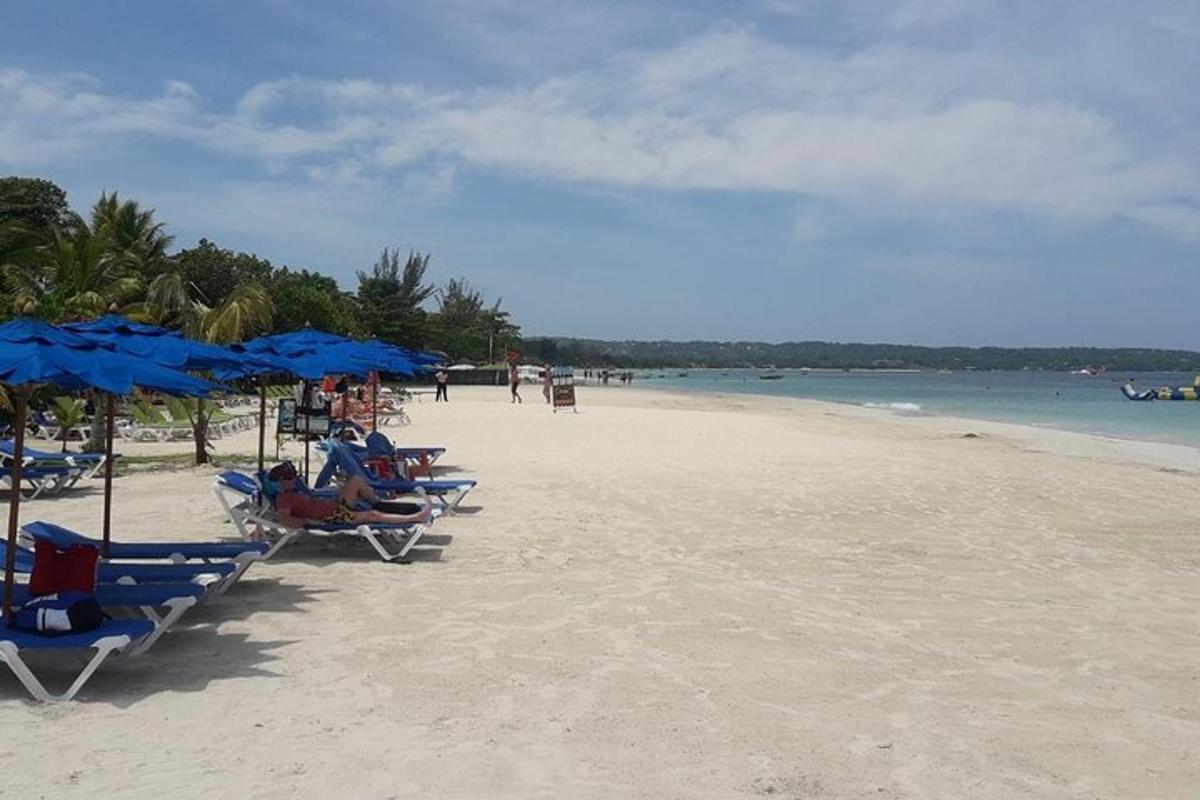 ein Strand mit Stühlen und blauen Sonnenschirmen und dem Meer