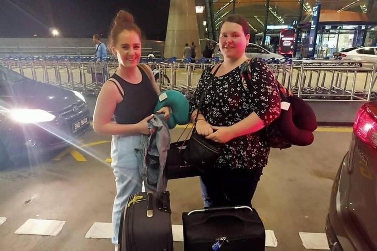 two women standing with their luggage at an airport