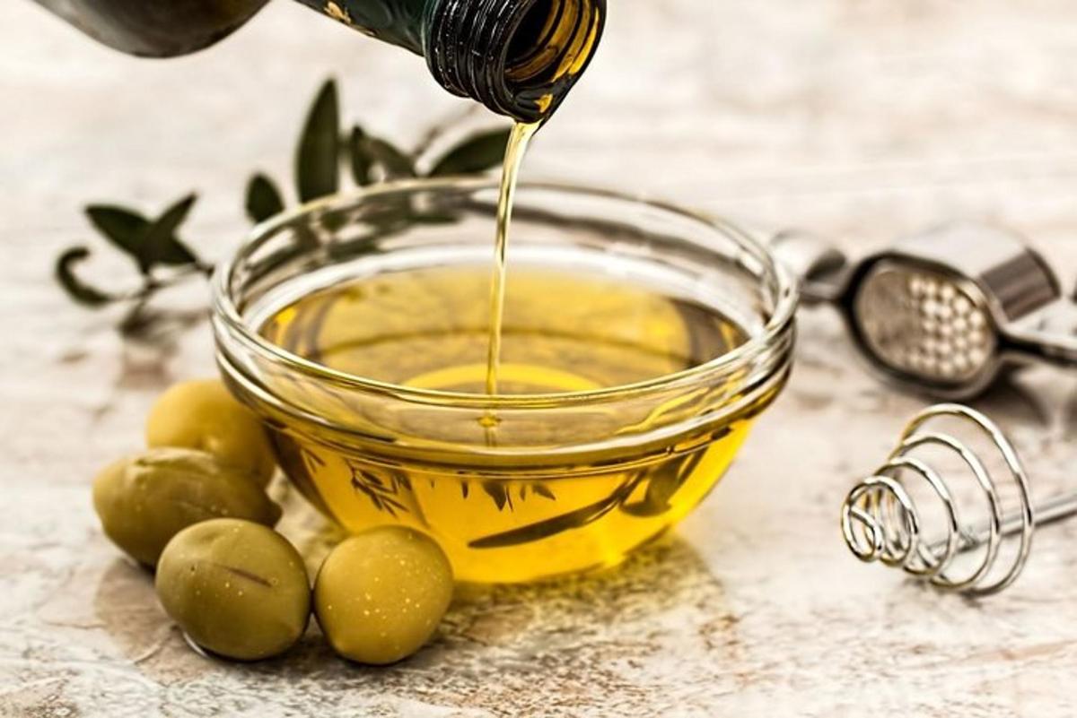 Una botella de aceite de oliva que se vierte en un recipiente con aceitunas.