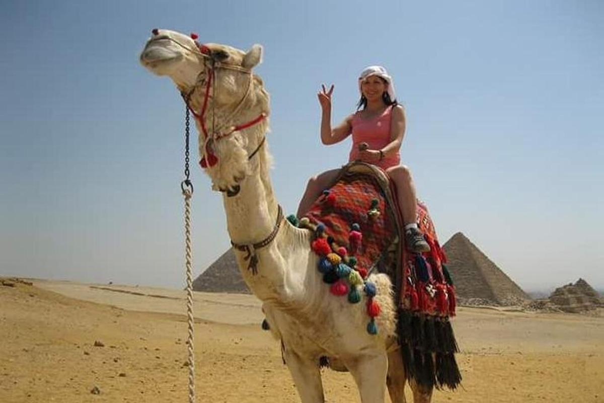 žena jedoucí na velbloudovi před pyramidami