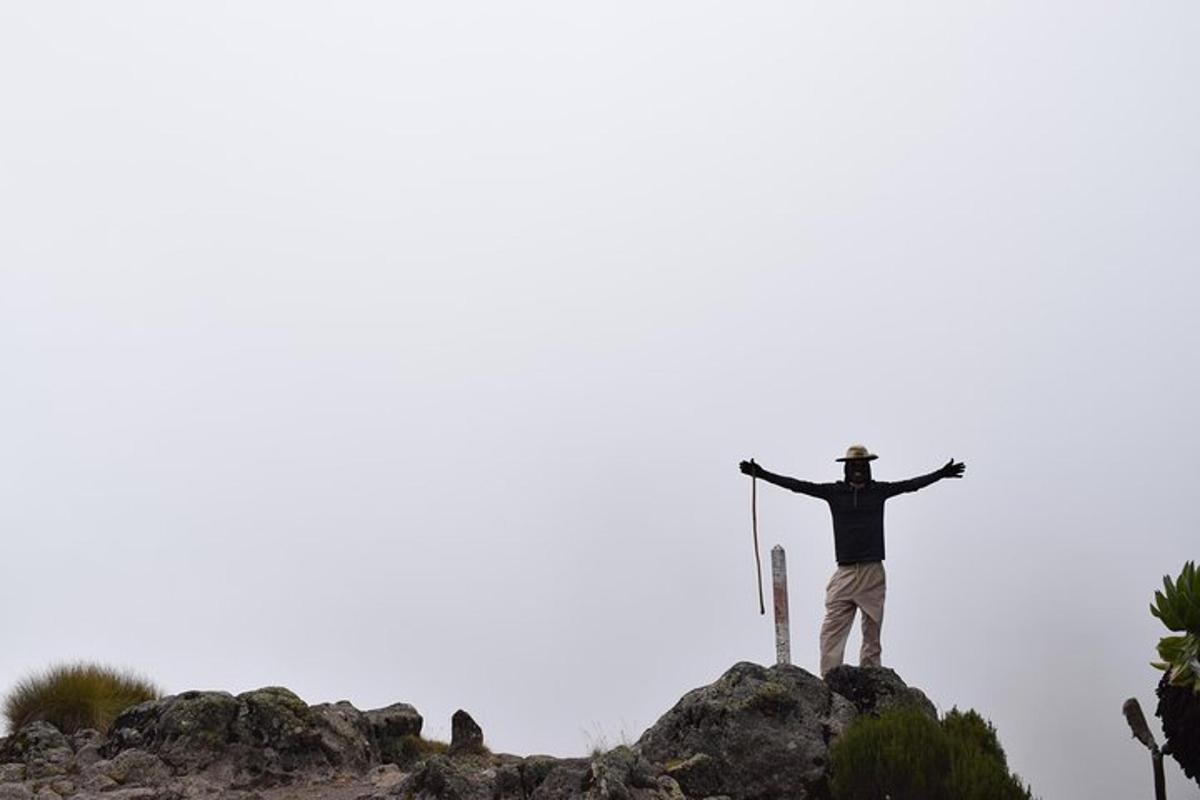 Ein Mann steht mit ausgestreckten Armen auf einem Berggipfel