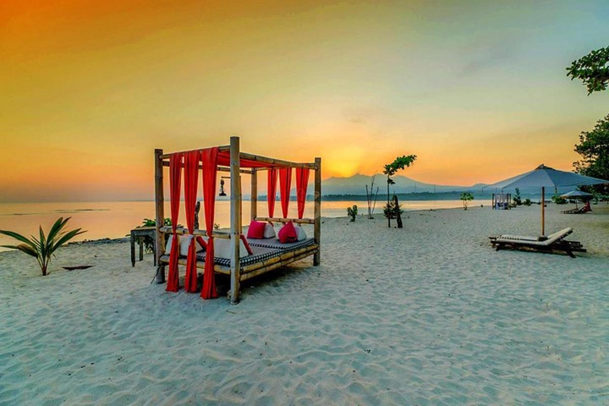 un letto su una spiaggia con il tramonto sullo sfondo