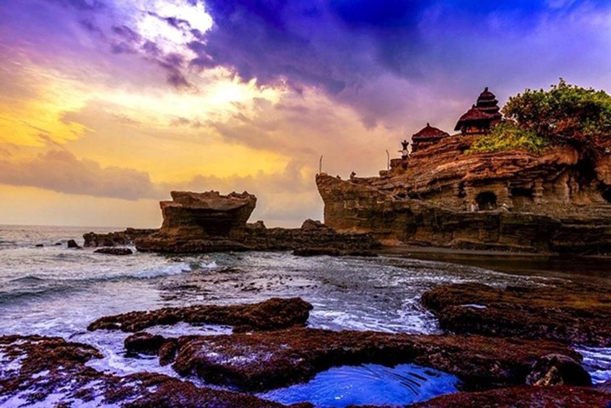 um pôr do sol sobre uma praia rochosa com um edifício nela