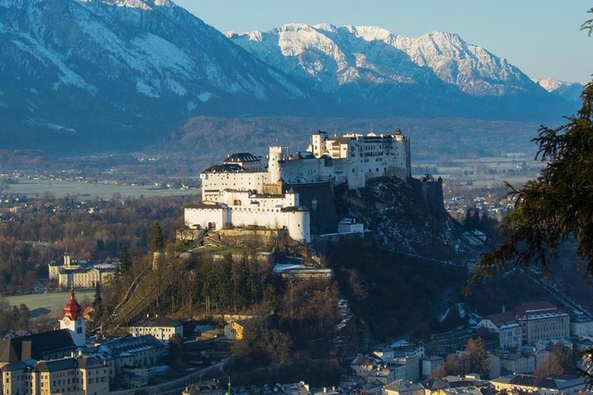 Un castillo en la cima de una colina con montañas cubiertas de nieve.