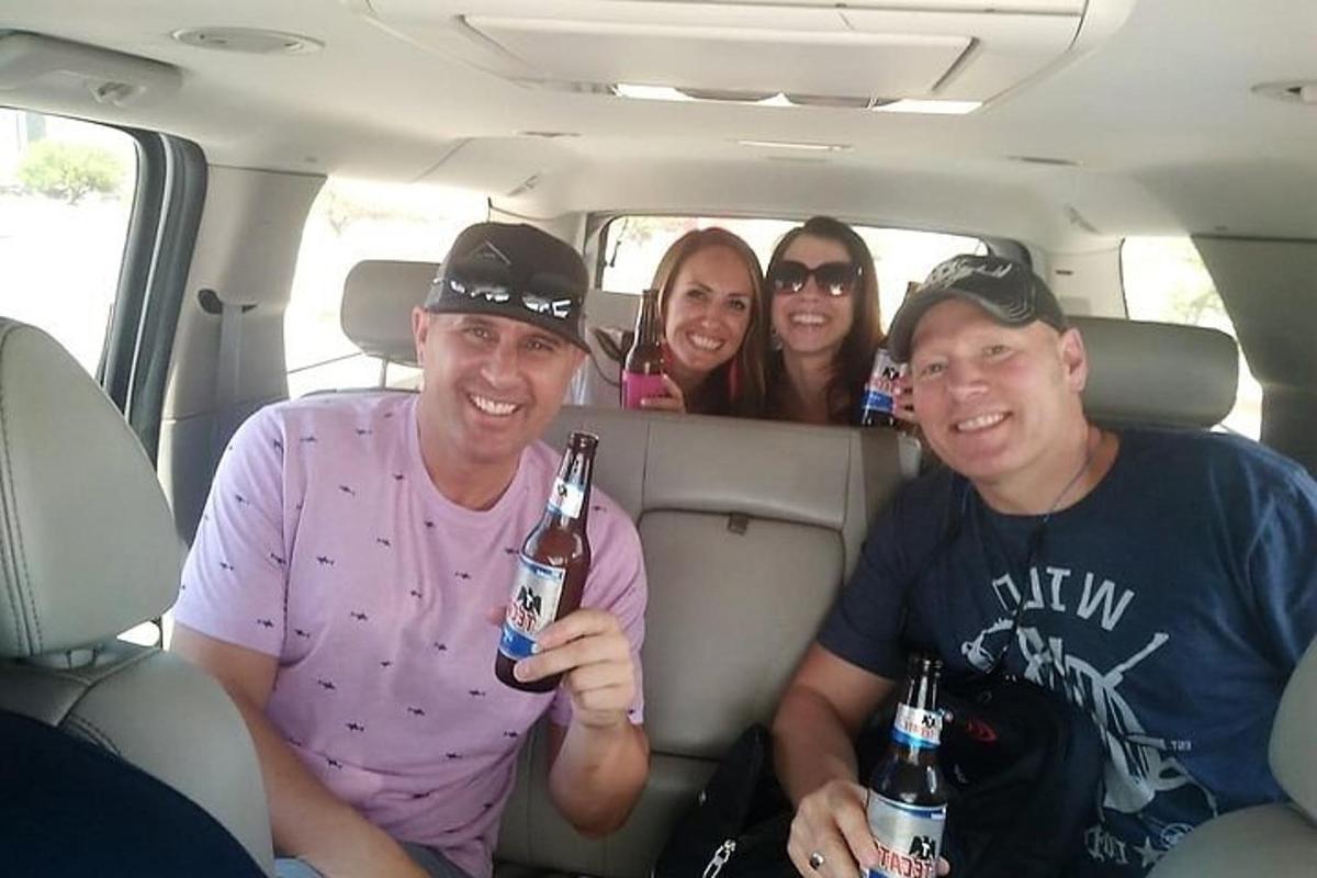 Un grupo de personas sentadas en un coche sosteniendo cerveza.