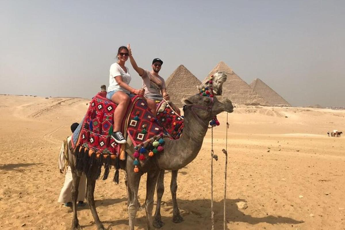 dva lidé jedoucí na velbloudovi před pyramidami