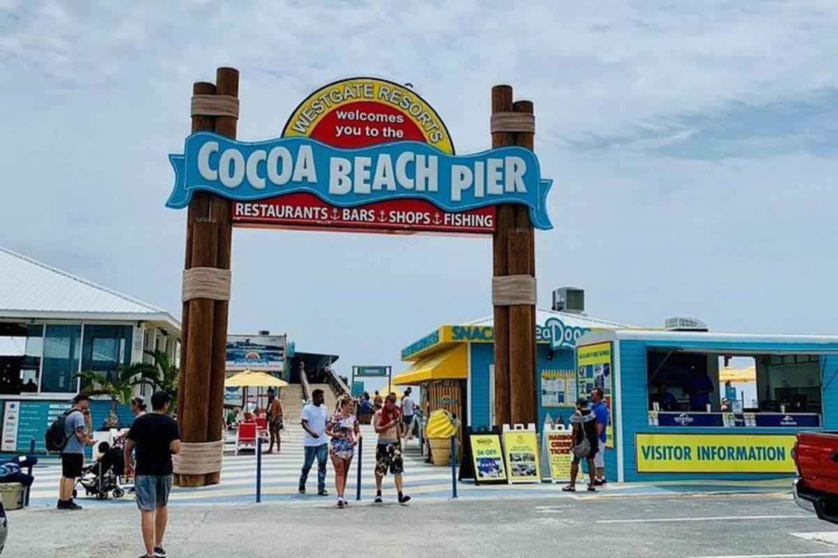 a sign for a beach pier with people standing around it