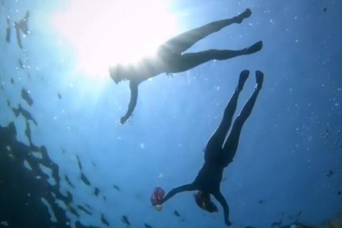 dua orang berenang di dalam air dengan matahari di belakang mereka