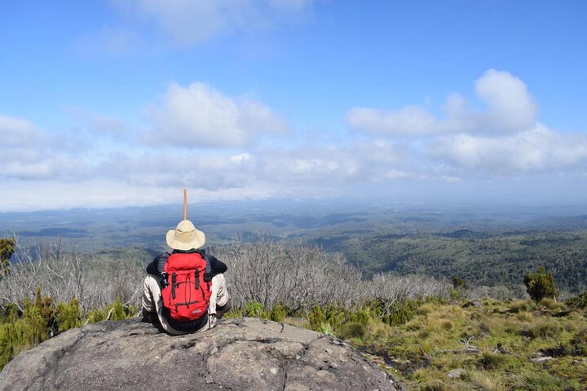 seseorang yang duduk di atas batu dengan beg galas merah