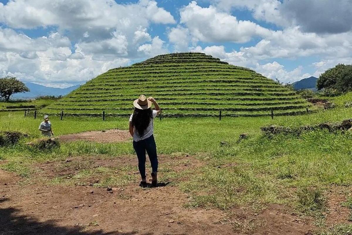a woman standing on a dirt road in front of a large hill