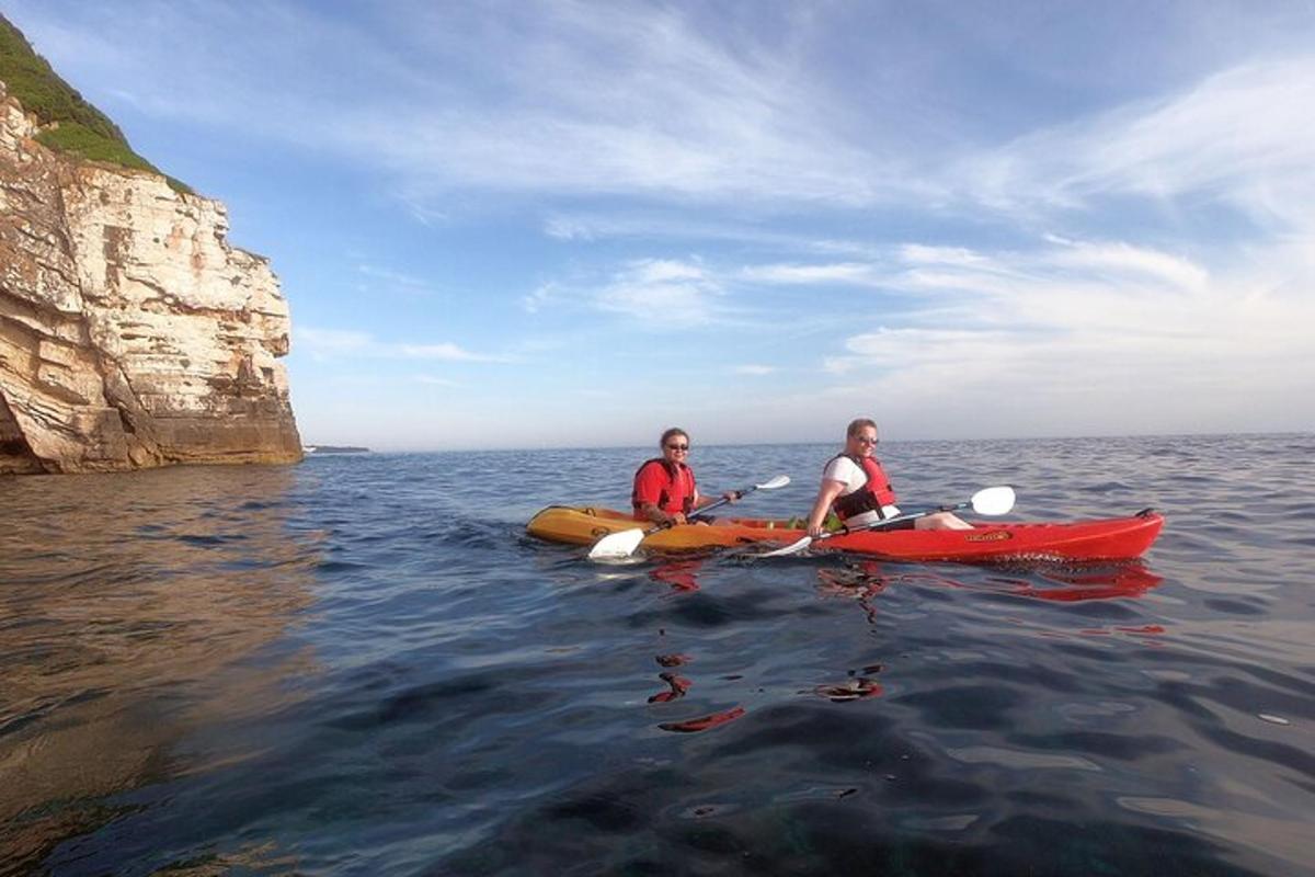 two people in kayaks in the water near a cliff