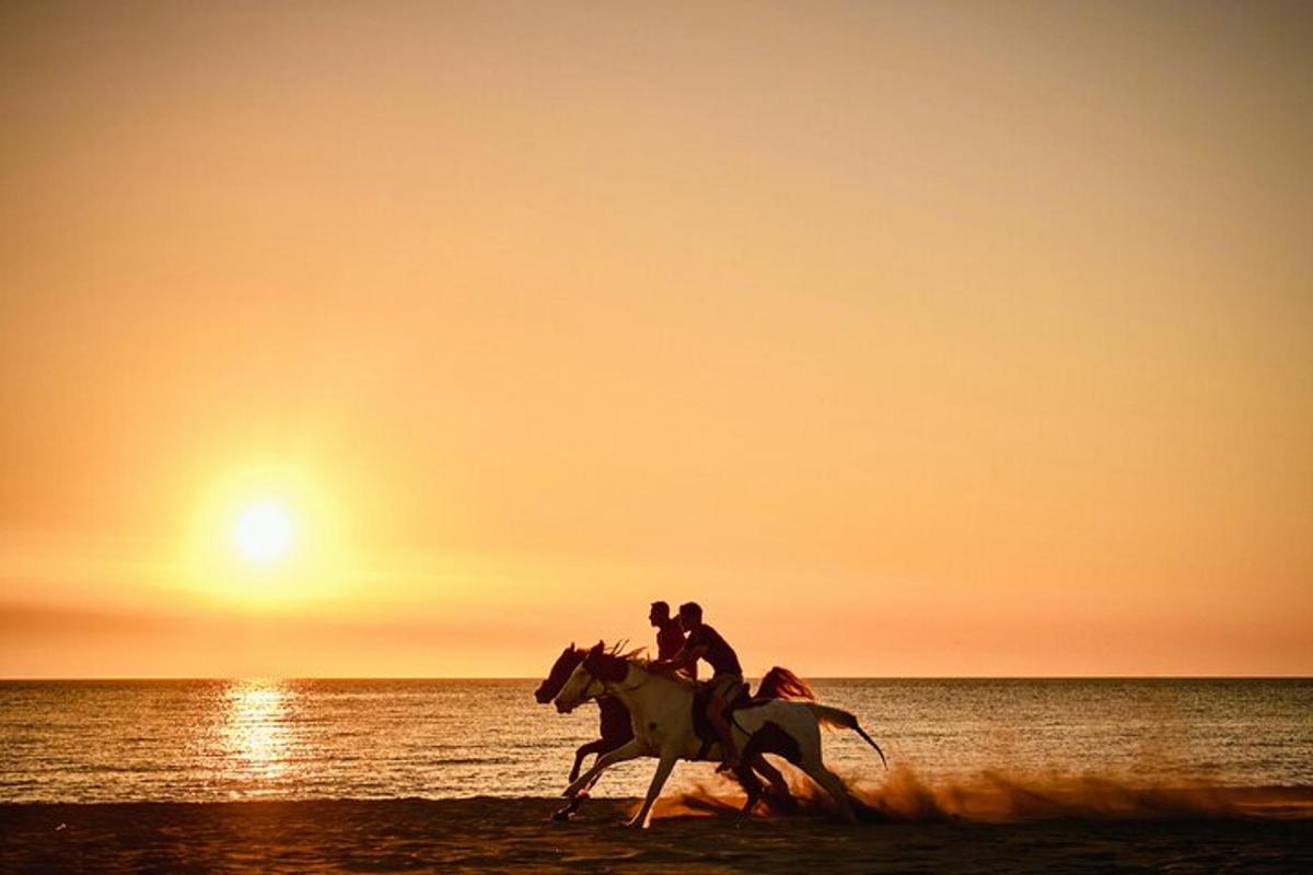 to personer som rir på hester på stranden ved solnedgang