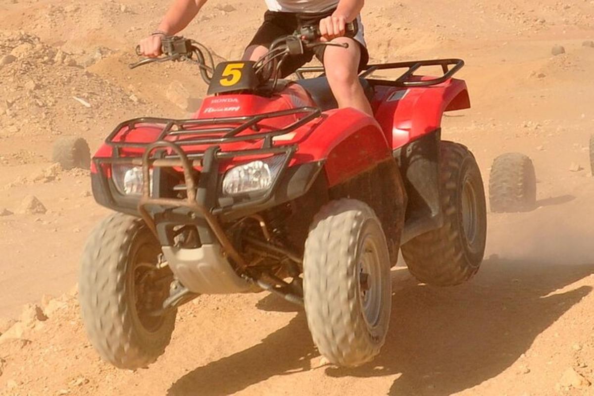 una persona che guida un quad rosso nello sporco