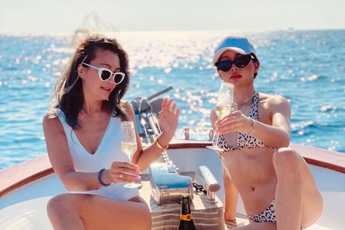 duas mulheres de biquíni sentadas em um barco com bebidas