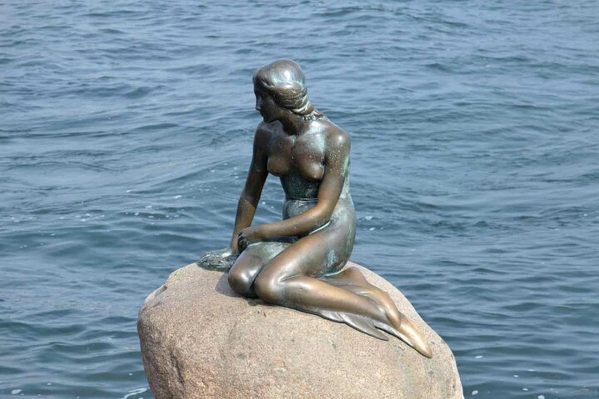 en statue av en kvinne som sitter på en stein i vannet