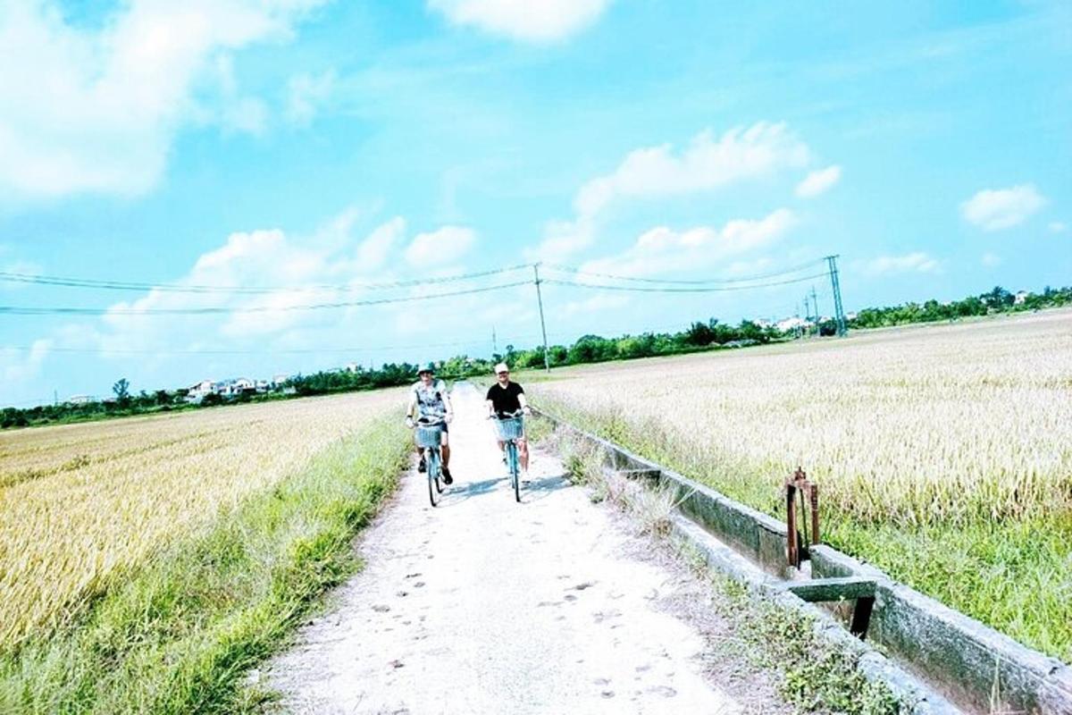 dva lidé jedoucí na kolech po prašné cestě přes pole