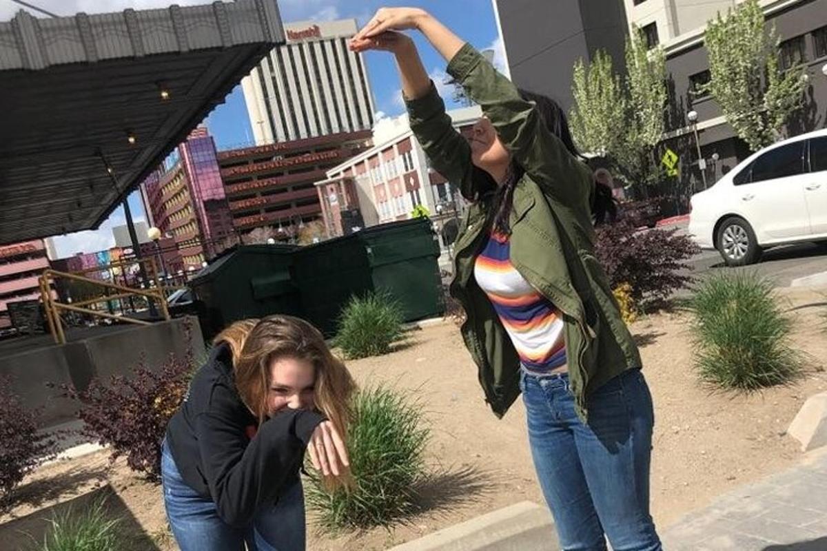 Dos chicas paradas en una acera con los brazos en el aire