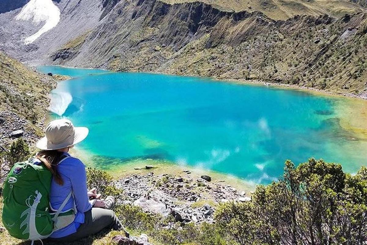 uma mulher sentada no topo de uma montanha olhando para um lago