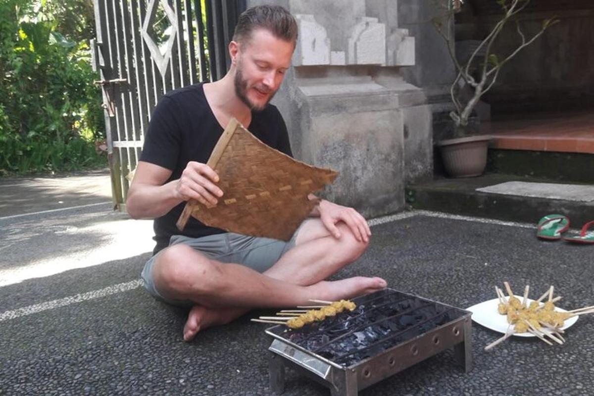 a man sitting on the ground next to a grill