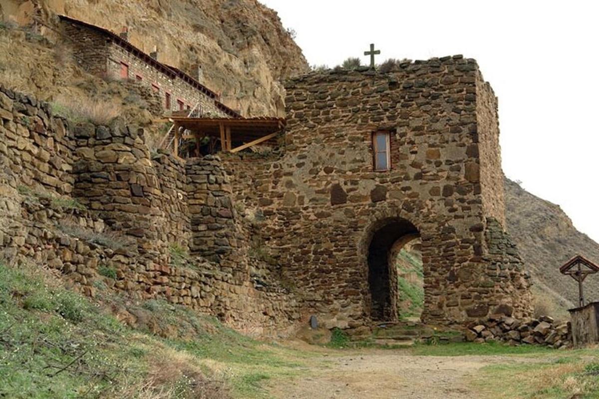 un vecchio edificio in pietra con una croce sul fianco di una collina