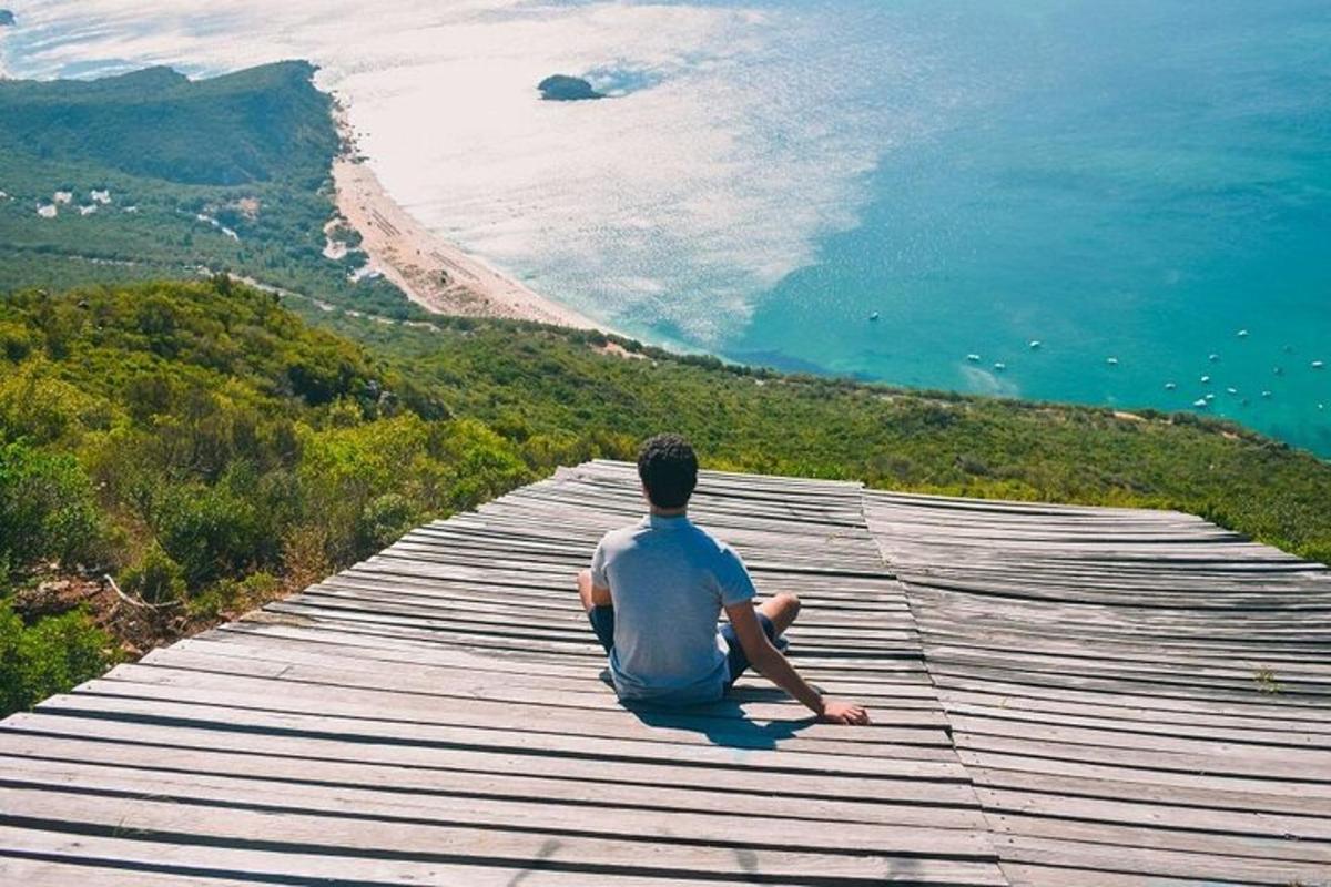 moški sedi na sprehajališču in gleda na ocean