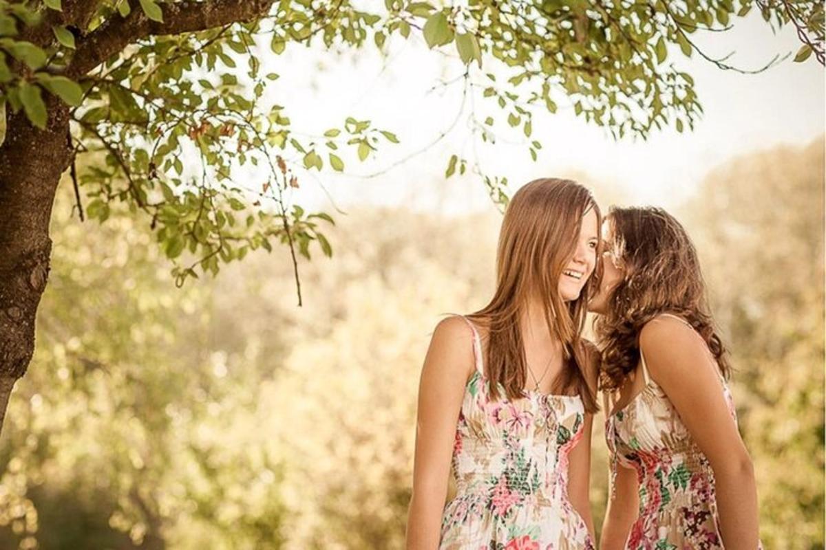 Dos mujeres jóvenes susurrándose al oído bajo un árbol