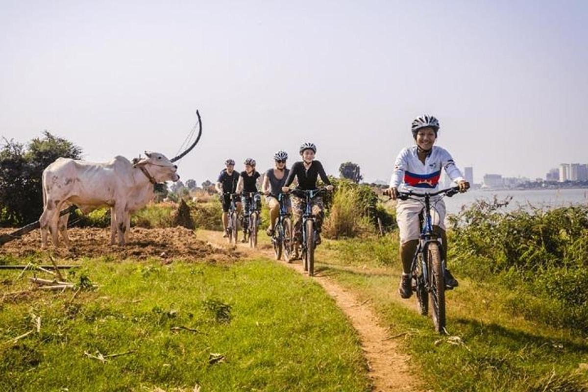 skupina ľudí jazdiacich na bicykloch po prašnej ceste s kravou