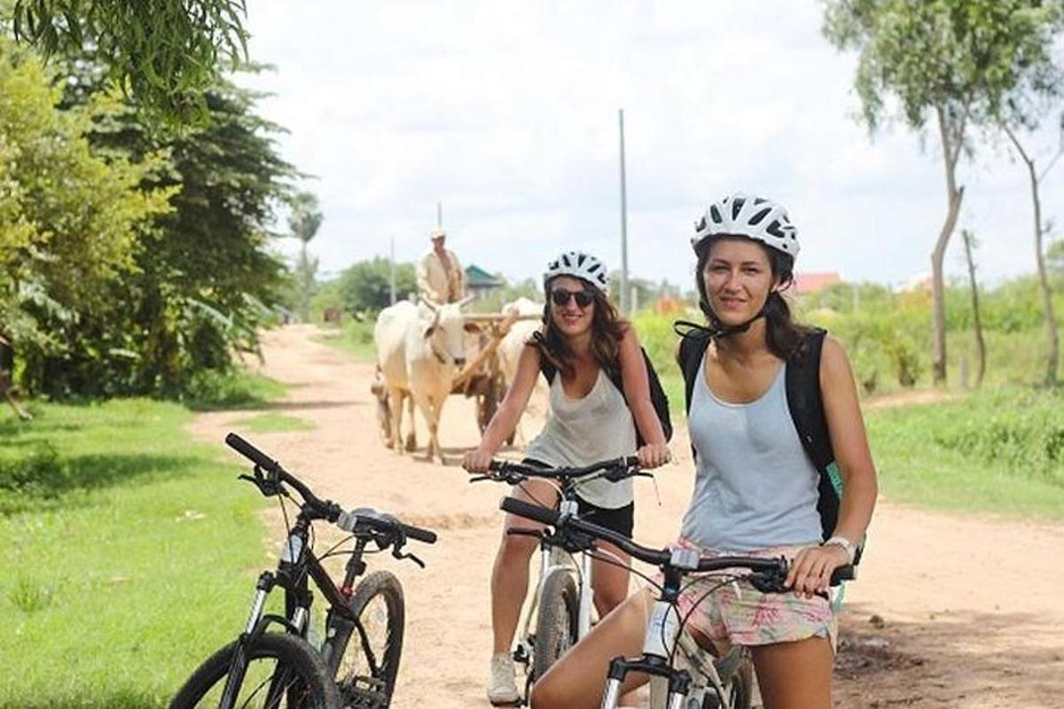 dve ženy jazdiace na bicykloch po prašnej ceste s kravami