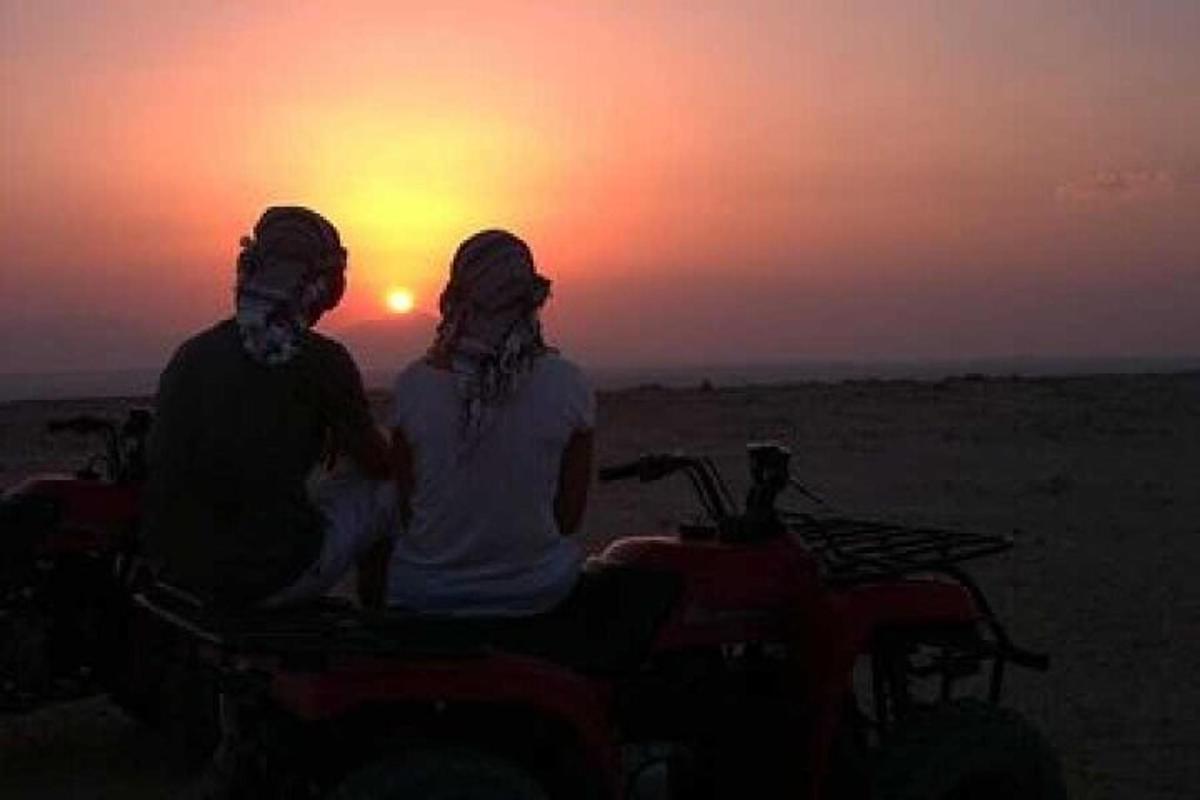 due persone sedute su un quad che guardano il tramonto
