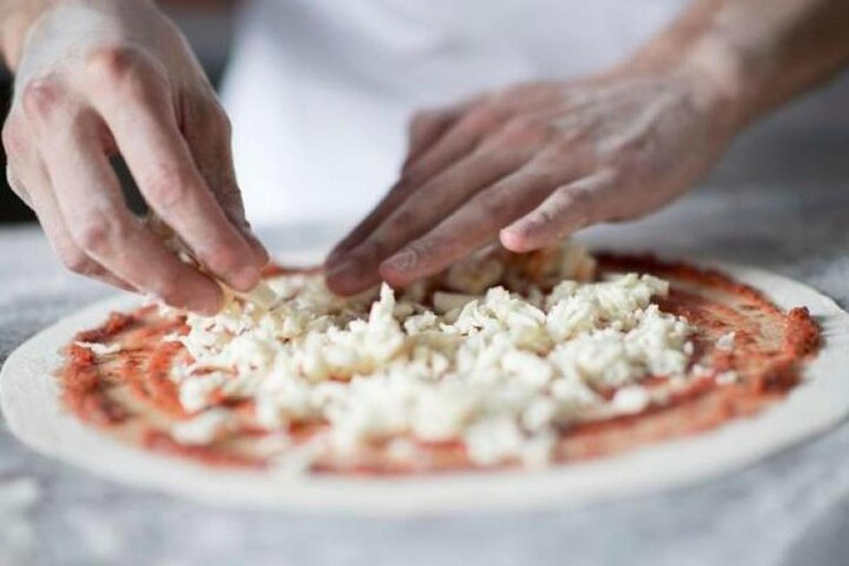 maður sem setur álegg á pizzu á disk
