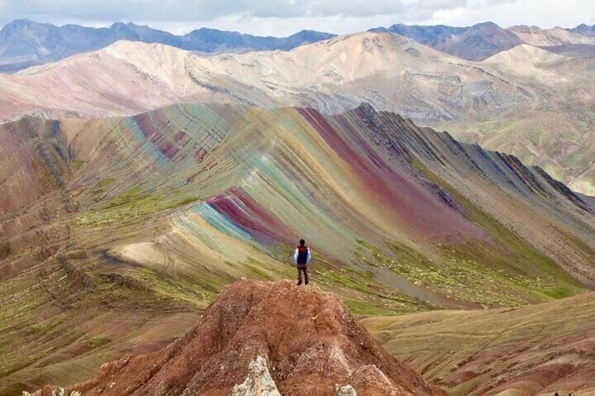 una persona parada en la cima de una montaña con un arcoíris