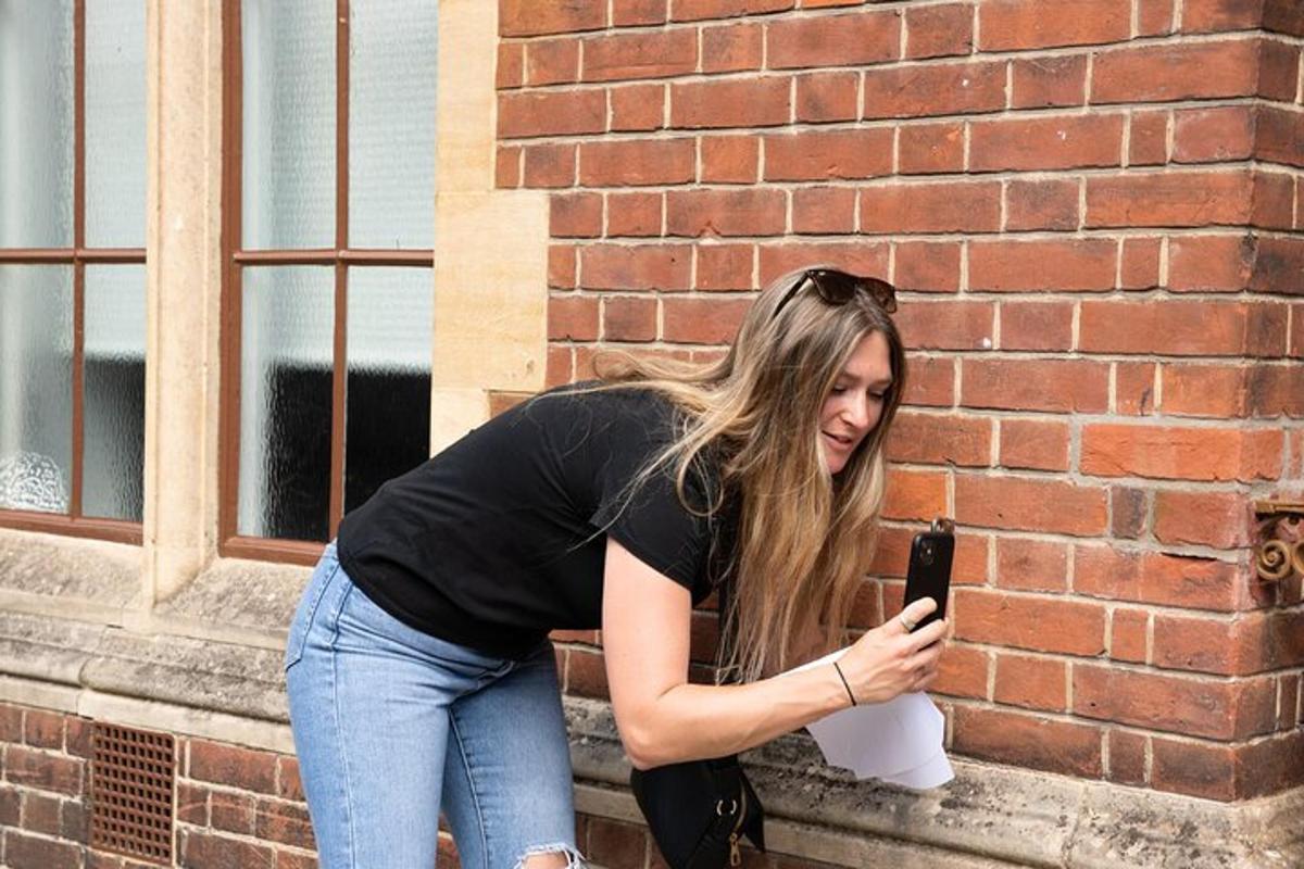 egy nő egy téglafalnak támaszkodva nézi a mobiltelefonját