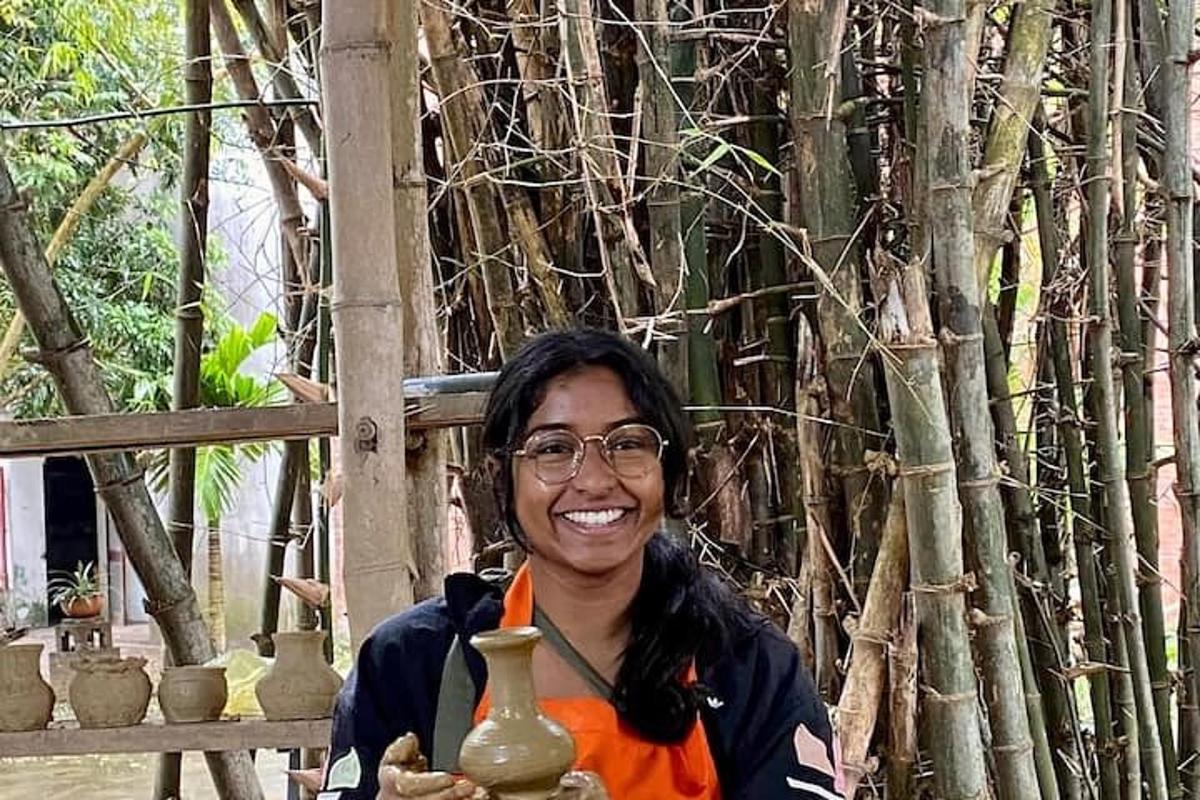 Una mujer sosteniendo jarrones frente a un árbol.