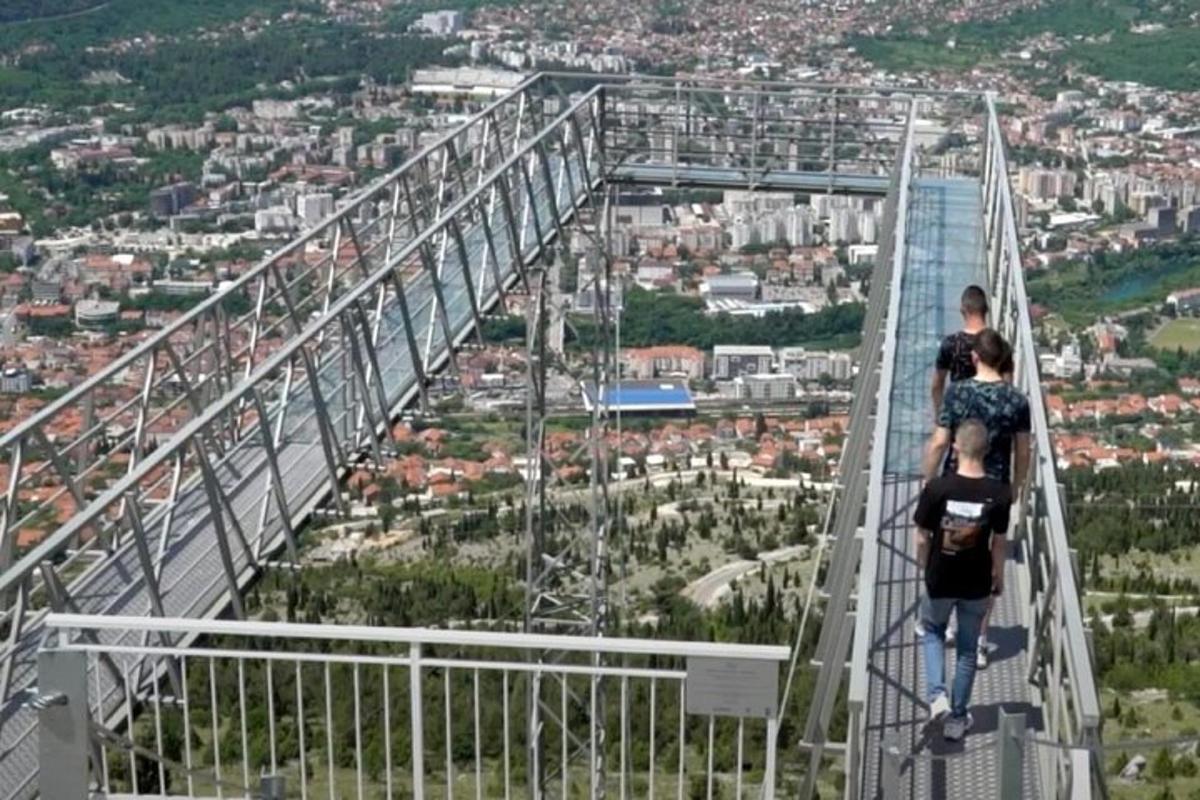 dva lidé jdoucí po visutém mostě nad městem