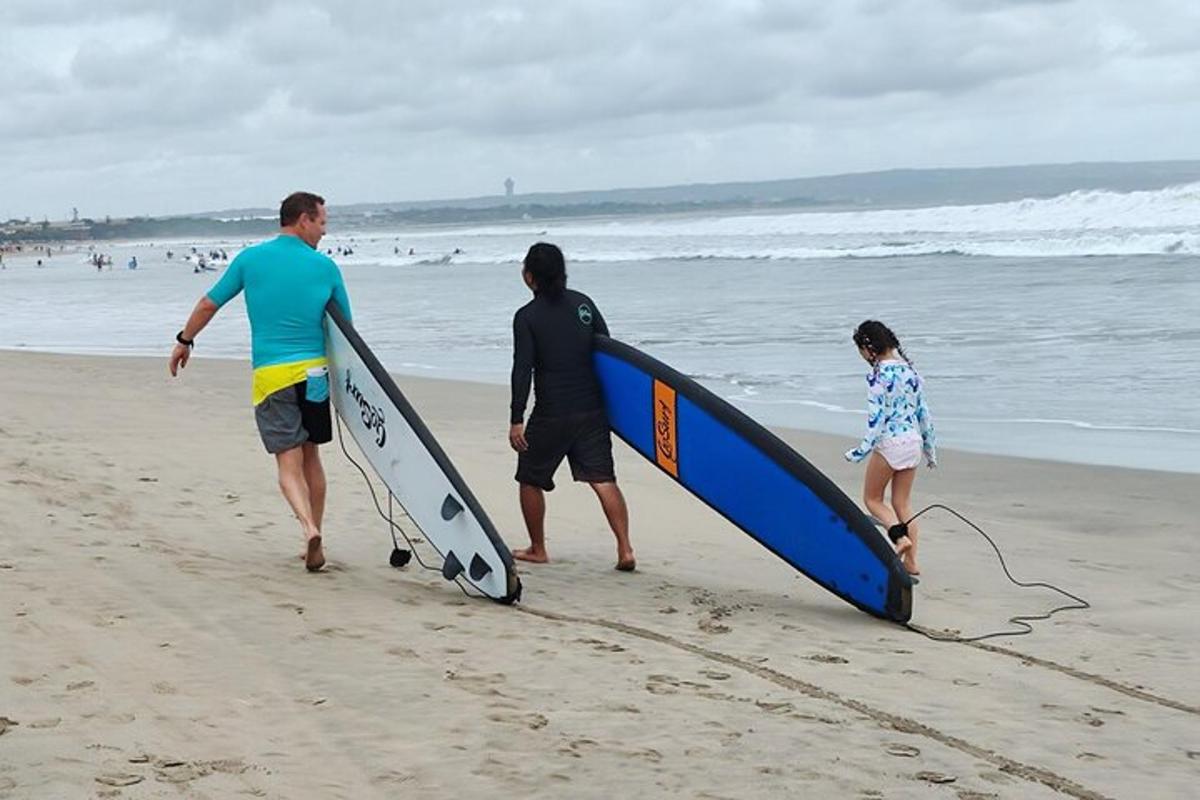 two men and a girl walking on the beach with surfboards