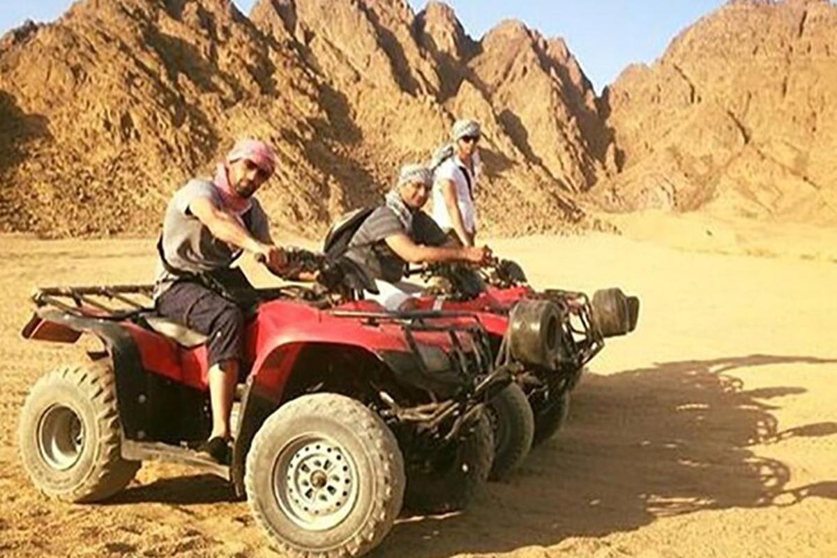 three men riding on a four wheeler in the desert