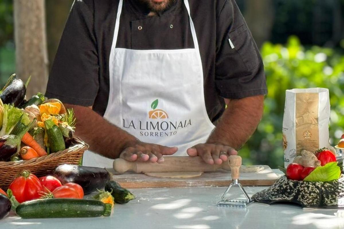 un home amb un davantal blanc dret al costat d'una taula amb verdures
