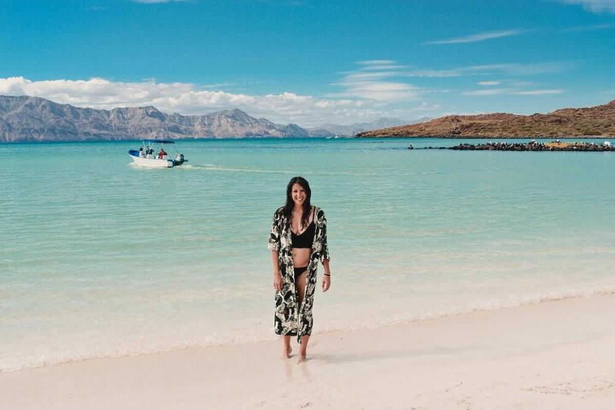 a woman standing on a beach with a boat in the water