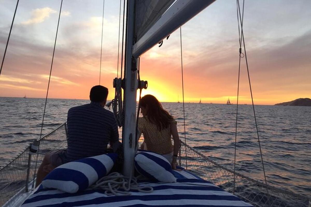 a man and woman sitting on a sail boat at sunset