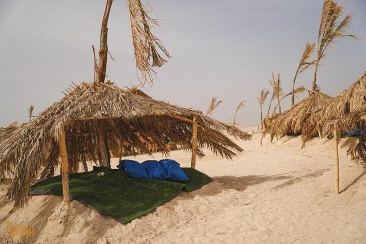 Una playa con una sombrilla de paja y dos carpas azules.