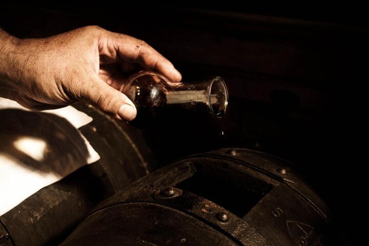 La mano de una persona sostiene una botella sobre un objeto metálico.