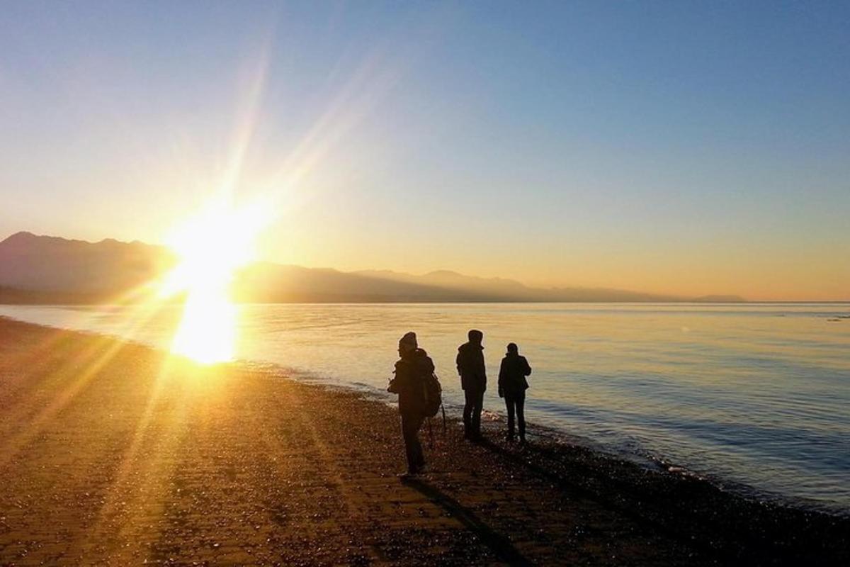 tre persone in piedi sulla spiaggia a guardare il tramonto