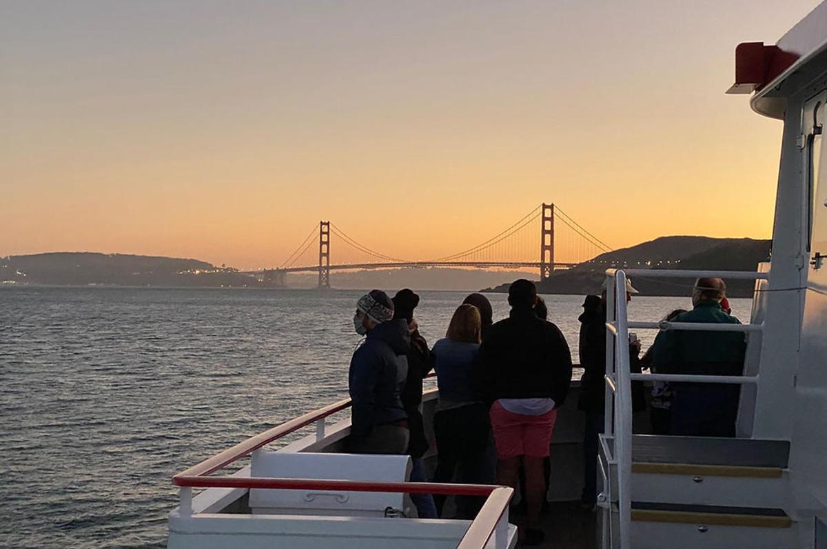 a group of people standing on a boat looking at the golden gate bridge